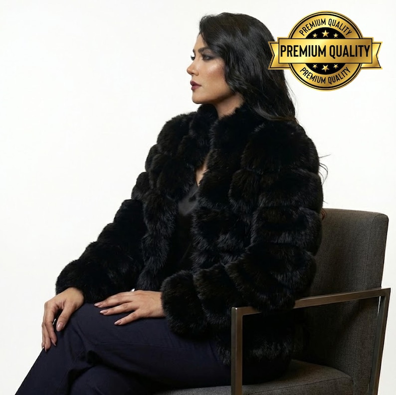 May include: A black fur coat with a round collar. The coat is worn by a person sitting in a gray chair. A gold seal with the words "Premium Quality" is in the upper right corner.