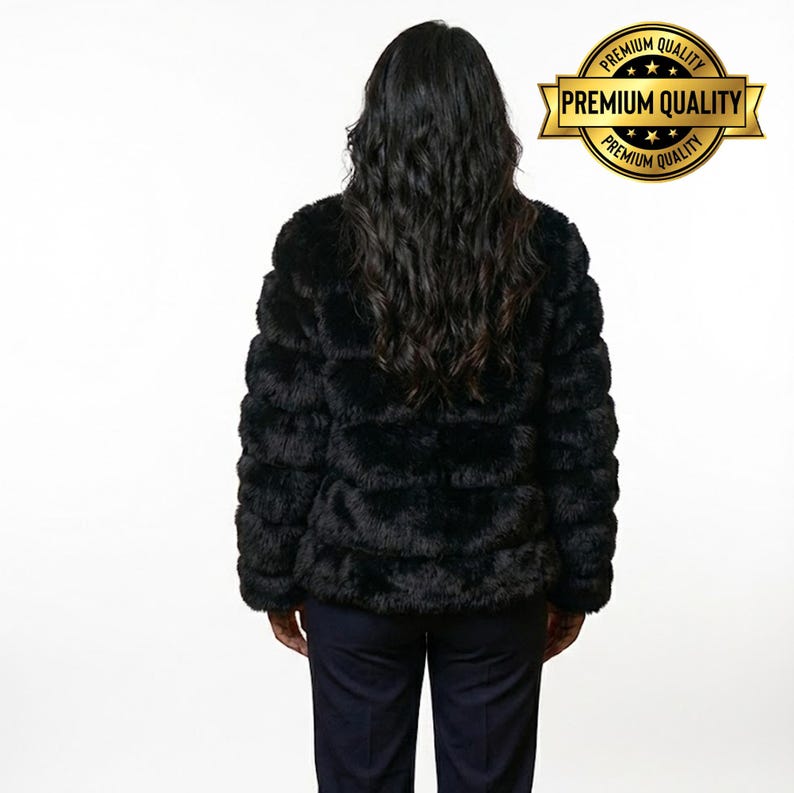 May include: A black faux fur jacket with a horizontal ribbed design. The jacket is worn over dark blue pants. A gold-colored emblem with the words "Premium Quality" is visible.