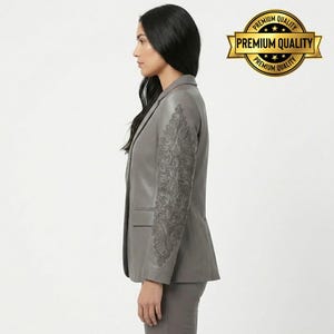 Pode incluir: Um blazer de couro cinza com detalhes bordados intrincados na manga. O blazer tem um design cl&aacute;ssico sob medida com lapela entalhada e fecho de um bot&atilde;o. A imagem tamb&eacute;m inclui um par de cal&ccedil;as cinza combinando.