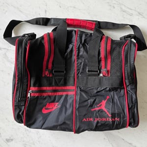 Pu&ograve; includere: Borsa da viaggio nera e rossa con i loghi Nike e Air Jordan. La borsa ha una tracolla nera e dettagli rossi. Ha un manico con impugnatura imbottita rossa. Diversi scomparti con cerniera.