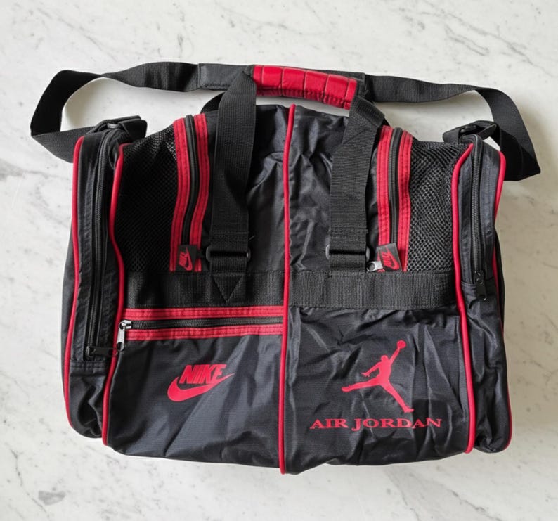 Pu&ograve; includere: Borsa da viaggio nera e rossa con i loghi Nike e Air Jordan. La borsa ha una tracolla nera e dettagli rossi. Ha un manico con impugnatura imbottita rossa. Diversi scomparti con cerniera.