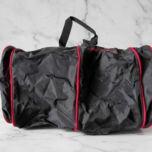 Pu&ograve; includere: Borsa da viaggio nera con finiture rosse e manico nero. La borsa sembra essere realizzata in un materiale leggero, forse nylon. La borsa &egrave; su una superficie di marmo bianco.