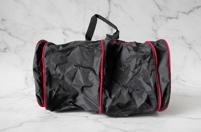 Pu&ograve; includere: Borsa da viaggio nera con finiture rosse e manico nero. La borsa sembra essere realizzata in un materiale leggero, forse nylon. La borsa &egrave; su una superficie di marmo bianco.