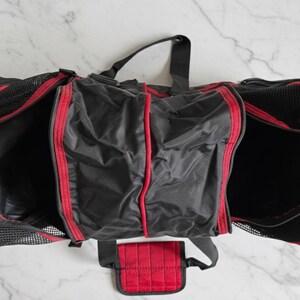 Pu&ograve; includere: Borsa da viaggio nera e rossa con pi&ugrave; scomparti. La borsa ha un esterno in rete nera con finiture e dettagli rossi. La borsa ha un manico superiore e una tasca rossa staccabile. La borsa &egrave; aperta, rivelando l'interno.