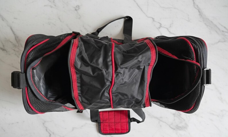 Pu&ograve; includere: Borsa da viaggio nera e rossa con pi&ugrave; scomparti. La borsa ha un esterno in rete nera con finiture e dettagli rossi. La borsa ha un manico superiore e una tasca rossa staccabile. La borsa &egrave; aperta, rivelando l'interno.