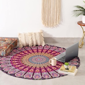 Può includere: Un arazzo mandala rotondo con un intricato motivo floreale nei toni del viola, blu e oro. Un laptop, una tazza, libri e una piccola pianta sono sopra. Sono presenti anche due cuscini color crema con frange e un cuscino da pavimento.