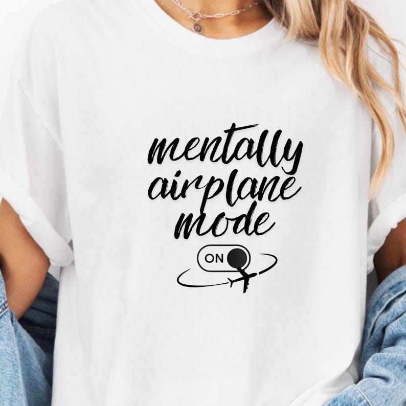 Może przedstawiać: Biała koszulka z czarnym napisem "mentally airplane mode". Poniżej znajduje się grafika samolotu z napisem "ON" w okręgu.