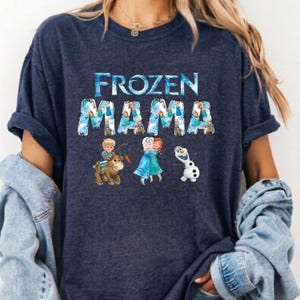 Pu&ograve; includere: T-shirt blu navy con la scritta "FROZEN MAMA" in un font acquerello blu. Il design include illustrazioni dei personaggi del film Frozen, come Anna, Elsa, Olaf e Kristoff. Una maglietta casual e confortevole.