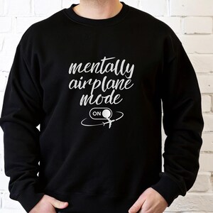 Może przedstawiać: Czarna bluza z białym napisem "mentally airplane mode" i grafiką samolotu. Słowo "ON" znajduje się pod grafiką samolotu. Bluza jest w stylu z okrągłym dekoltem.