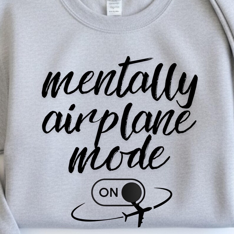 Może przedstawiać: Jasnoszara bluza z napisem "mentally airplane mode" w czarnym skrypcie. Poniżej tekst znajduje się grafika samolotu i przełącznika "ON", r&oacute;wnież w kolorze czarnym. Bluza ma swobodny styl.