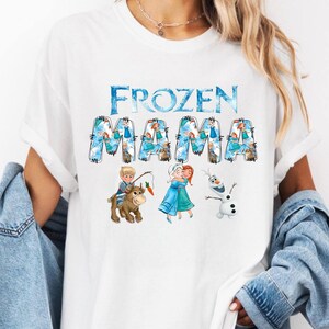 Pu&ograve; includere: T-shirt bianca con la scritta "FROZEN MAMA" in blu, con illustrazioni dei personaggi del film Frozen. La maglietta ha girocollo e maniche corte. Il design include immagini di Anna, Elsa, Olaf e Kristoff.