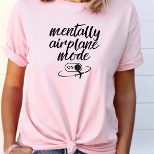 Może przedstawiać: Jasnor&oacute;żowa koszulka z czarnym napisem "mentally airplane mode". Poniżej znajduje się grafika samolotu ze słowem "ON" w okręgu.