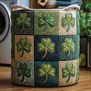 Può includere: Un cesto portaoggetti rotondo e decorativo con un motivo a trifoglio trapuntato. Il cesto presenta un motivo ripetuto di trifogli verdi su un patchwork di quadrati verdi, blu e beige. Ha due manici in corda ed è adatto per la biancheria o lo stoccaggio.