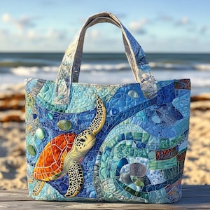 Puede incluir: Un bolso tote acolchado con un diseño de tortuga marina. El bolso tiene una combinación de colores azul y turquesa con una aplicación detallada de una tortuga. Las asas y el cuerpo del bolso están hechos de tela con un patrón acolchado. El fondo muestra una escena de playa.