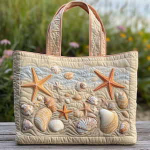 May include: Quilted tote bag with a beach design, featuring seashells and starfish. The bag has a beige background with blue and tan accents, and a quilted pattern. The handles are a light pink colour.