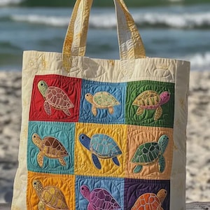 Puede incluir: Bolso tote color crema con un diseño de patchwork que presenta nueve cuadrados coloridos, cada uno con una tortuga marina bordada. El bolso tiene asas acolchadas amarillas y un borde a juego, ideal para la playa.