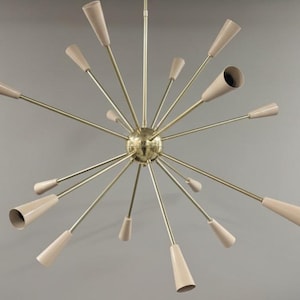 Può includere: Un lampadario moderno della metà del secolo con un design a forma di stella. Presenta più bracci che si estendono da una sfera centrale, ciascuno con un paralume a forma di cono beige. I bracci e la sfera centrale hanno una finitura dorata.
