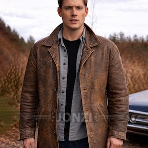 Op de afbeelding: Bruine leren jas met een knoopsluiting en een kraag. De jas heeft een versleten, verweerde uitstraling. De afbeelding toont ook een zwart shirt en een grijs shirt onder de jas. De merknaam "JONZI" is zichtbaar.