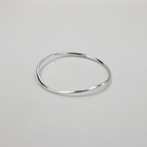 May include: A silver-colored, thin, wavy bracelet. The bracelet is a simple, elegant design, with a smooth, polished surface. The bracelet is circular and appears to be made of metal. The bracelet is on a light-colored background.