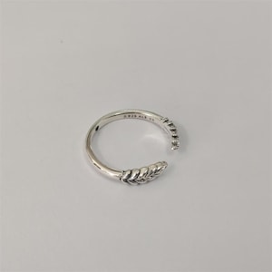 Peut inclure: Bague ouverte en argent avec un motif de feuille et de petites pierres. La bague est marquée "S 925 ALE 54". L'anneau est posé sur un fond blanc.