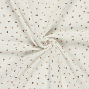 May include: A white fabric featuring a repeating pattern of small, light brown five-petalled flowers. The material is gathered in the centre, creating soft, radiating folds that highlight the texture and the consistent floral print design.