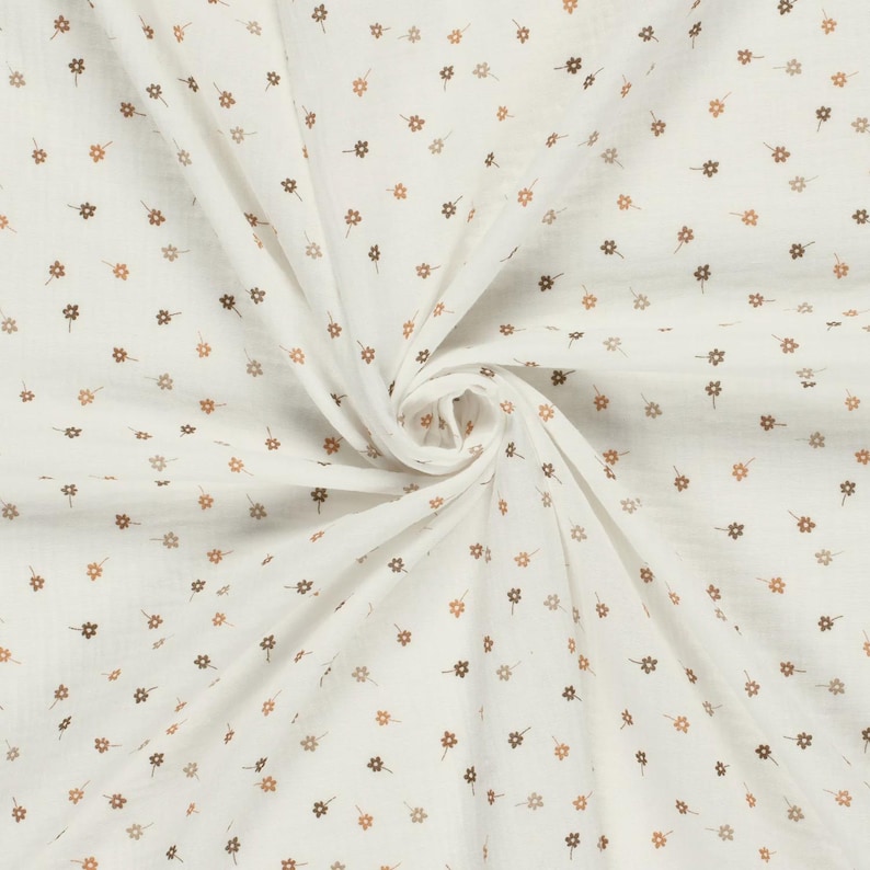 May include: A white fabric featuring a repeating pattern of small, light brown five-petalled flowers. The material is gathered in the centre, creating soft, radiating folds that highlight the texture and the consistent floral print design.
