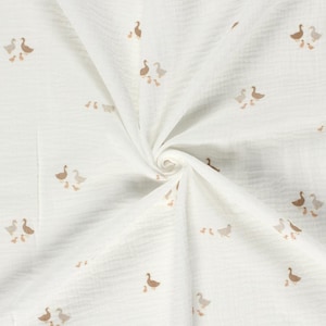 May include: A white muslin fabric featuring a repeating pattern of small brown and light grey geese and goslings. The textile has a crinkled, textured surface with a soft, gathered appearance radiating from the centre of the folded material.
