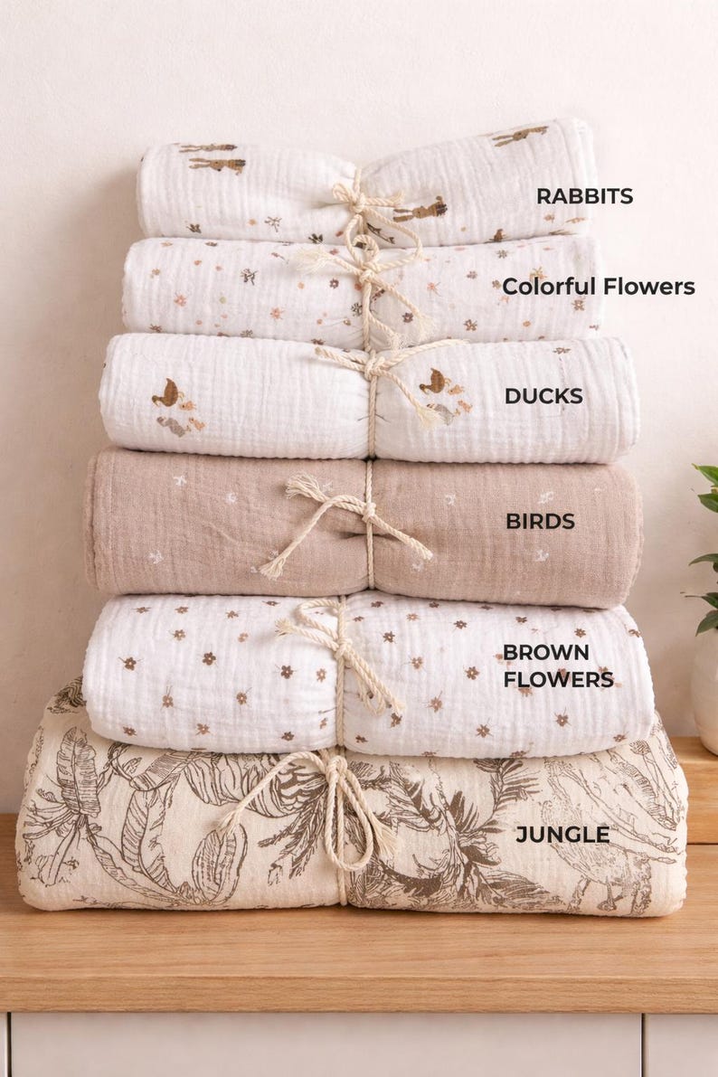 May include: A stack of six folded muslin blankets tied with twine. The patterns include rabbits, colourful flowers, ducks, birds, brown flowers, and a jungle print. Each blanket is labelled with its respective design name in black text on the right side.
