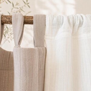 May include: Close-up of beige and white linen curtains hanging from a wooden rod. The beige curtains have fabric loops for hanging, while the white curtains are gathered at the top. The curtains are made of a textured fabric.