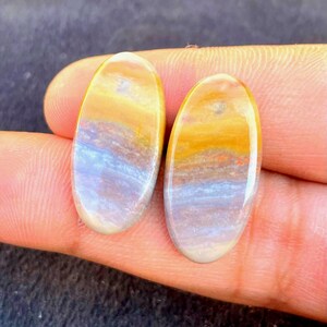 May include: Two oval-shaped cabochons with a smooth, polished finish. Each stone features horizontal bands of color, transitioning from a warm golden yellow at the top to a soft, muted lavender and light blue in the center, ending in a creamy white base.