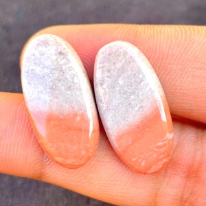 May include: Two oval-shaped cabochons featuring a smooth, polished surface with a distinct color gradient. Each piece transitions from a textured, light gray or white upper section to a solid, vibrant coral-orange lower section with a glossy finish.