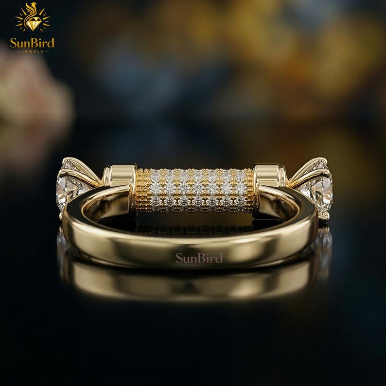 Puede incluir: Un anillo de oro con una barra central con diamantes y dos grandes gemas claras a cada lado. El anillo tiene un acabado pulido y el nombre de la marca "SunBird" est&aacute; grabado.