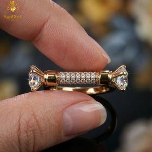 "Close-up of a woman's hand wearing a modern, horizontal bar gold ring with pave detailing and two clear end stones on her middle finger."