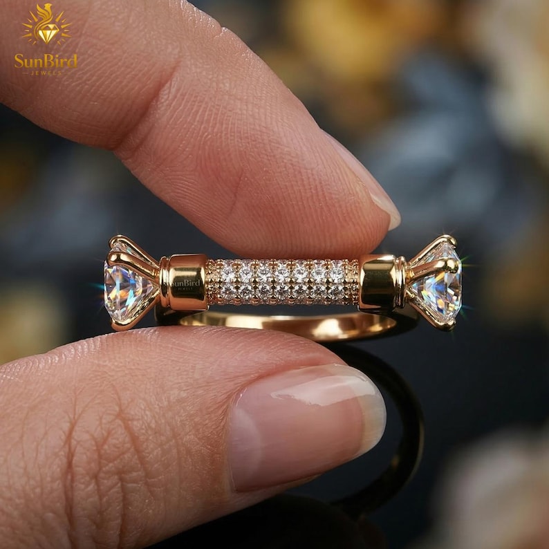 "Close-up of a woman's hand wearing a modern, horizontal bar gold ring with pave detailing and two clear end stones on her middle finger."