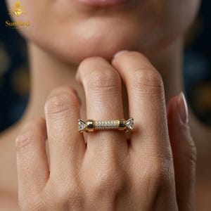 "Close-up of a woman's hand wearing a modern, horizontal bar gold ring with pave detailing and two clear end stones on her middle finger."