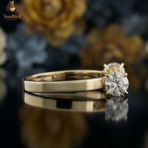 "Side perspective of a unique geometric gold ring resting on a dark surface with softly blurred flowers in the background, highlighting its candy-wrapper shape."