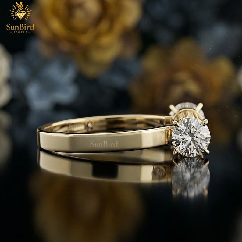 "Side perspective of a unique geometric gold ring resting on a dark surface with softly blurred flowers in the background, highlighting its candy-wrapper shape."
