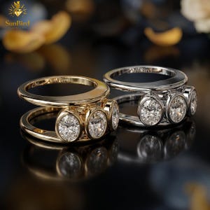 May include: Two rings, one in gold and one in silver, each featuring a double band design and three oval-cut clear stones set in a bezel style. The interior of each band is engraved with the text SunBird.