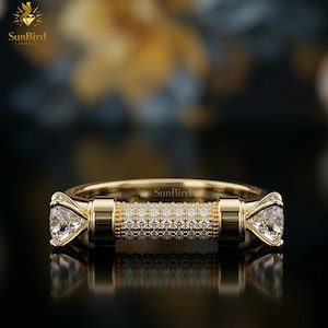 "Front view of a unique gold statement ring featuring a horizontal, cylinder-shaped bar encrusted with clear pave stones, finished with a larger faceted stone on each end against a dark background."