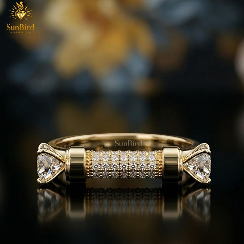 "Front view of a unique gold statement ring featuring a horizontal, cylinder-shaped bar encrusted with clear pave stones, finished with a larger faceted stone on each end against a dark background."