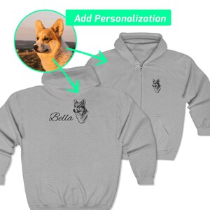 May include: A light gray zip-up hoodie with a black and white corgi sketch on the chest and a smaller version on the back. The word "Bella" is written in cursive below the corgi sketch. The image includes a corgi portrait and the text "Add Personalization".