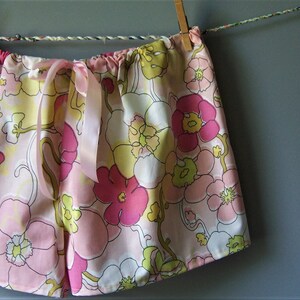 Op de afbeelding: Roze en gele pyjamabroek met bloemenprint en een satijnen strik.