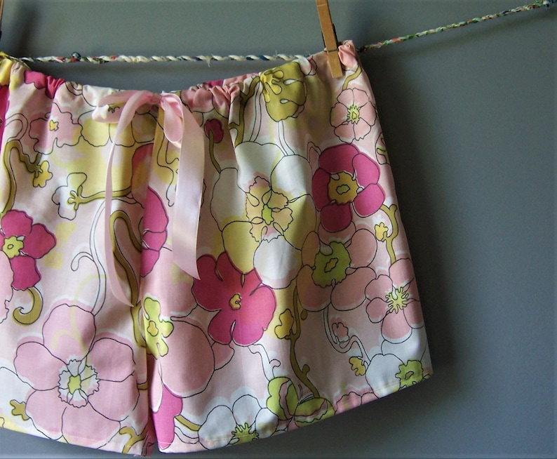 Op de afbeelding: Roze en gele pyjamabroek met bloemenprint en een satijnen strik.