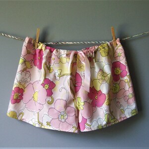 Op de afbeelding: Roze en gele pyjamabroek met bloemenprint en een satijnen strik. De broek hangt aan een waslijn.