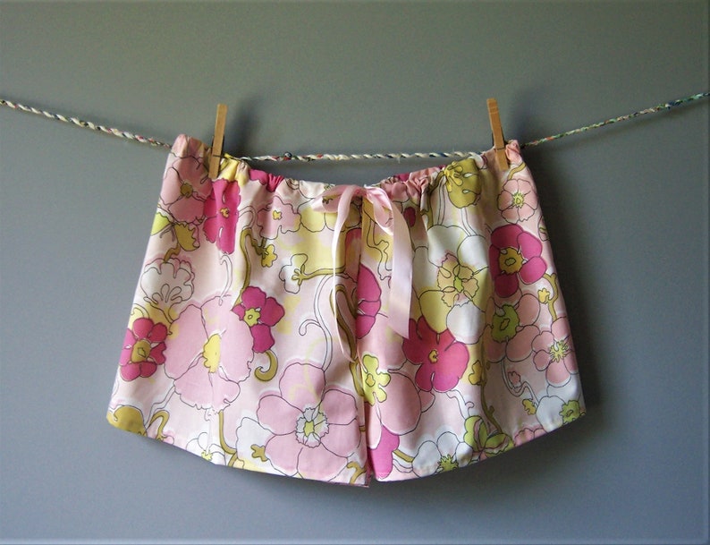 Op de afbeelding: Roze en gele pyjamabroek met bloemenprint en een satijnen strik. De broek hangt aan een waslijn.