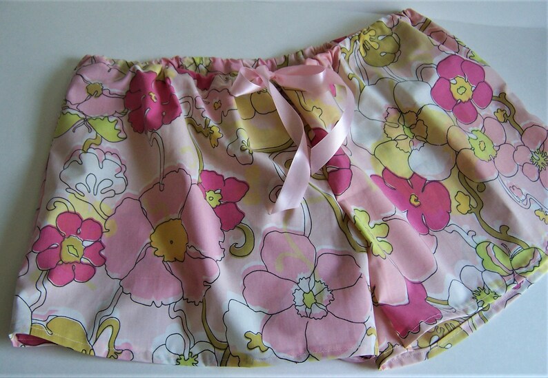 Op de afbeelding: Roze en gele pyjamabroek met bloemenprint en een roze satijnen strik aan de taille.