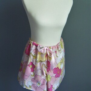 Op de afbeelding: Een roze en witte bloemenprint rok met een satijnen lint strik. De rok heeft een retro stijl uit de jaren 1970.