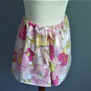 Op de afbeelding: Een roze en witte rok met bloemenprint en een satijnen strikband aan de taille.