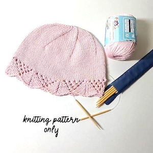 Puede incluir: Un gorro de punto rosa claro con un borde festoneado, una madeja de hilo rosa y agujas de tejer. El texto "knitting pattern only" está escrito en la imagen. El gorro es un artículo hecho a mano.
