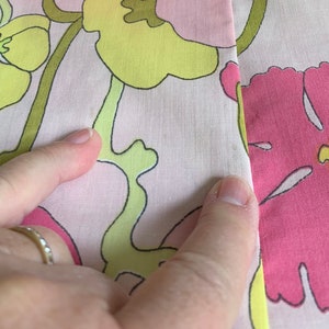 Op de afbeelding: Roze stof met een bloemenpatroon in tinten geel, groen en roze. De stof heeft een naad in het midden.